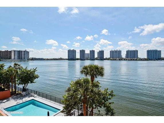 View of tall buildings across a body of water with a swimming pool in the foreground.