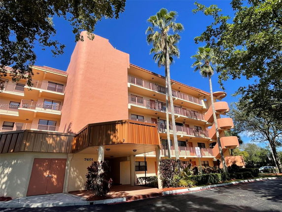 Front view of a multi-story building with balconies and palm trees.