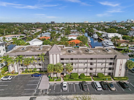 Front view of a multi-story building with a parking area and palm trees in front.
