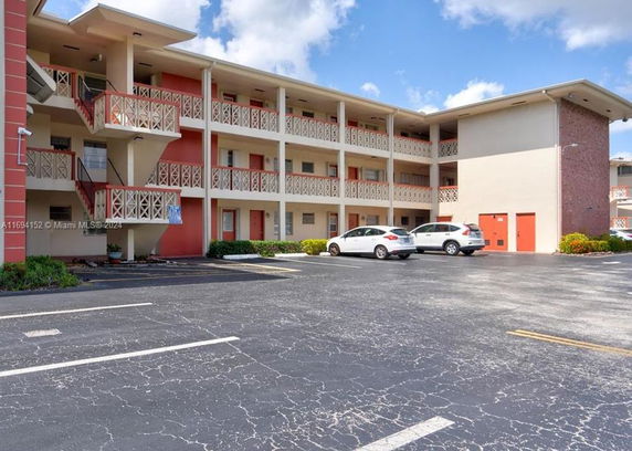 A three-story apartment building with balconies and outdoor parking spaces.