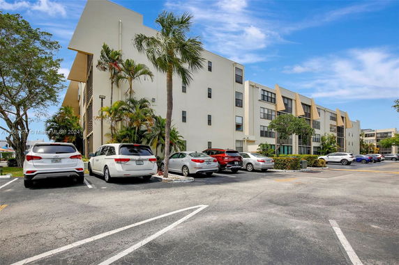 Outdoor parking area with multiple cars in front of a multi-story building.