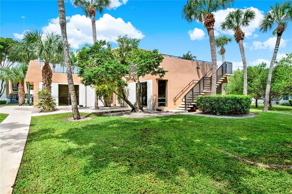 Front view of a two-story building with exterior stairs and surrounded by palm trees.
