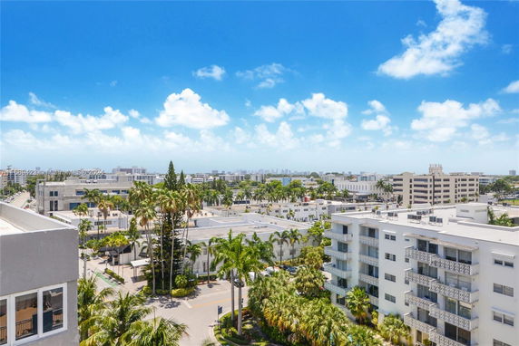 Panoramic view of multiple mid-rise buildings with balconies, surrounded by palm trees and a clear blue sky.