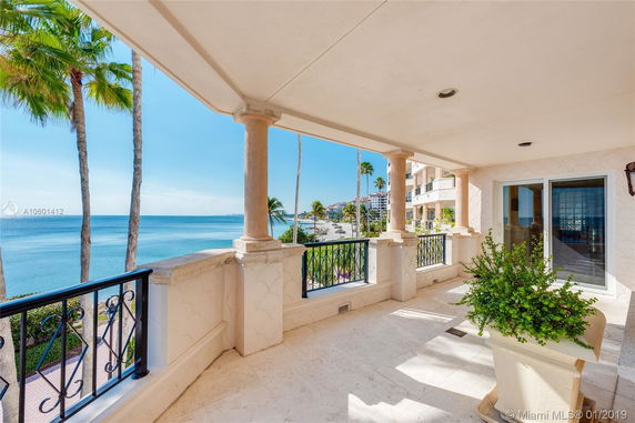 Covered balcony area with elegant columns and ornate railing overlooking a beach and ocean.