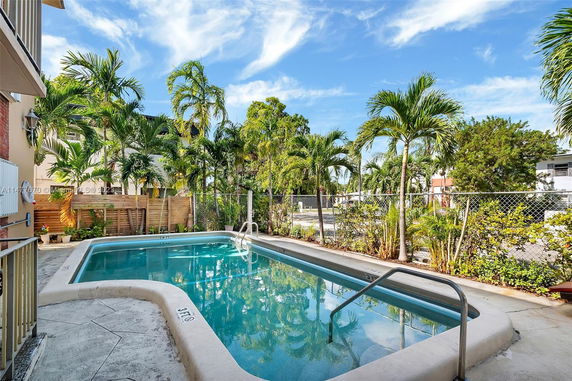 Outdoor swimming pool area with palm trees and a fenced perimeter.