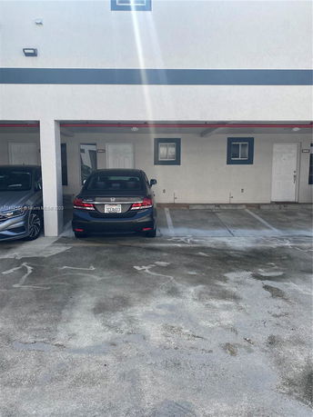 Outdoor parking area with parked cars in front of a building entrance.
