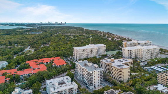 Aerial view of mid-rise buildings near a coastline with a city skyline in the distance.