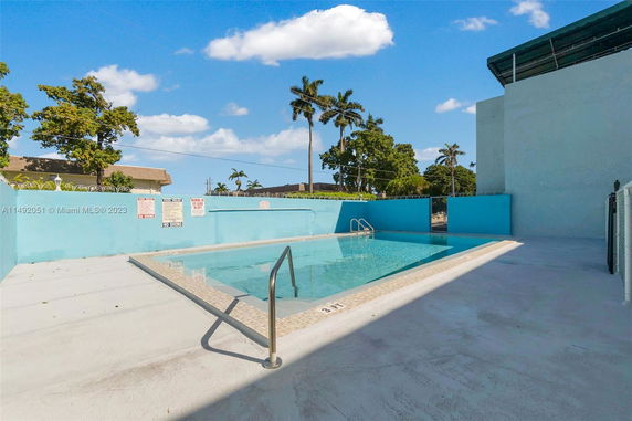 Outdoor swimming pool with surrounding blue walls and metal railing.