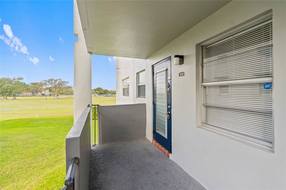 Exterior corridor with a closed door and windows, overlooking a grassy area.