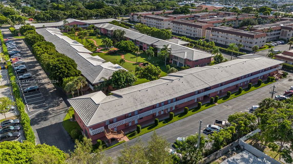 Aerial view of residential buildings surrounded by greenery and parking areas.
