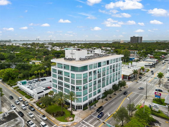 Aerial view of a multi-story building with a flat roof, featuring large windows and surrounded by streets and greenery.