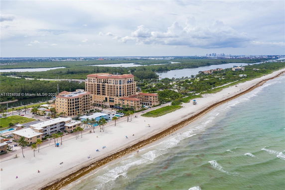 Aerial view of a beachfront building complex with surrounding landscape and beach.