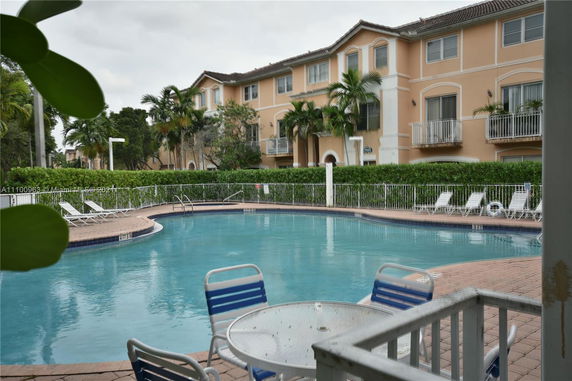 Outdoor swimming pool with surrounding lounge chairs and multi-story residential building in the background.