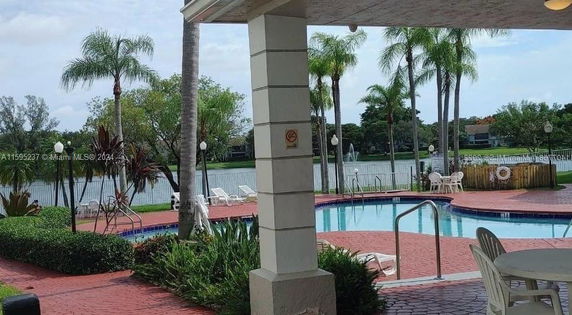 Outdoor swimming pool area with palm trees and lake view.