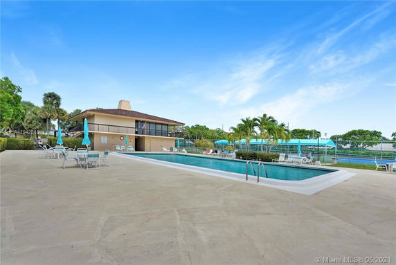View of a two-story building with a swimming pool and tennis courts nearby.