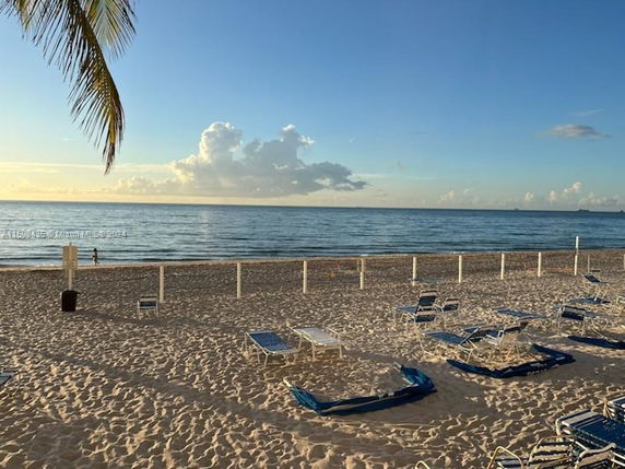 Beach view with lounge chairs and calm ocean with clear skies.