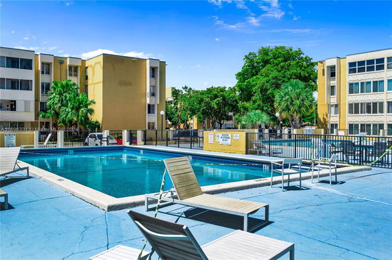 Outdoor swimming pool area with lounge chairs surrounded by multi-story buildings.