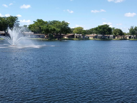 View of a lake with a water fountain and houses in the background.