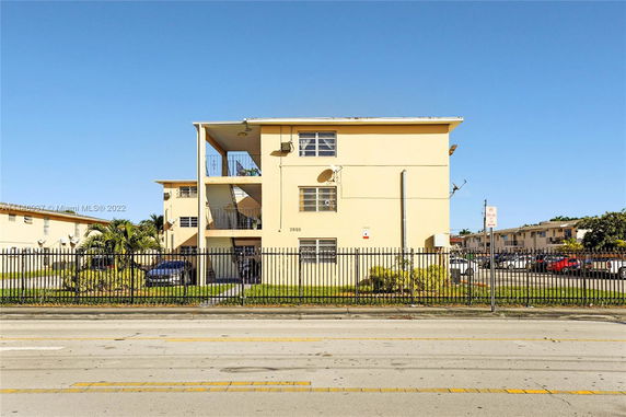 Front view of a three-story apartment building with balconies and a gated street entrance.