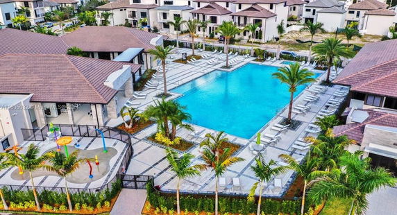 Aerial view of a swimming pool with surrounding lounging area and adjacent playground in a residential complex.