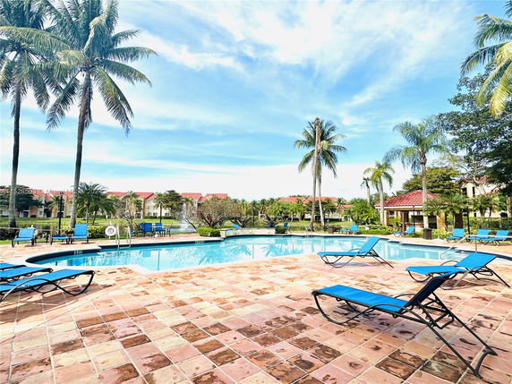 Outdoor swimming pool with lounge chairs and palm trees surrounding it.