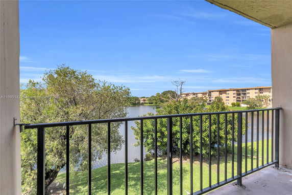 View from a building balcony overlooking trees and a water body with buildings in the background.