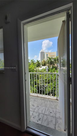 View from an open door showing a balcony with a railing and distant buildings with a blue sky.