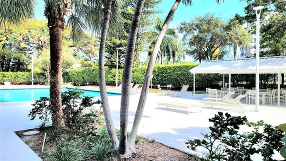 Outdoor swimming pool area with lounge chairs and tables under a canopy.