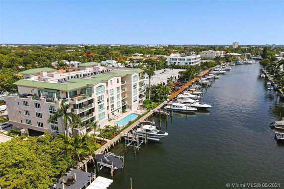 Aerial view of a multi-story apartment building next to a waterway with docks and boats.