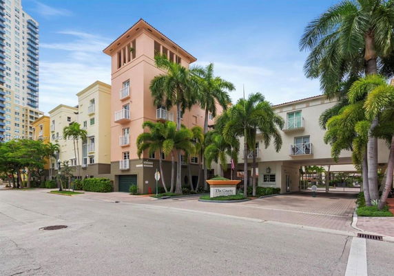 Front view of a multi-story building with balconies and palm trees.