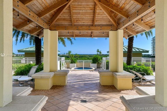 Patio area with a wooden gazebo covering a hot tub, surrounded by lounge chairs and palm trees.