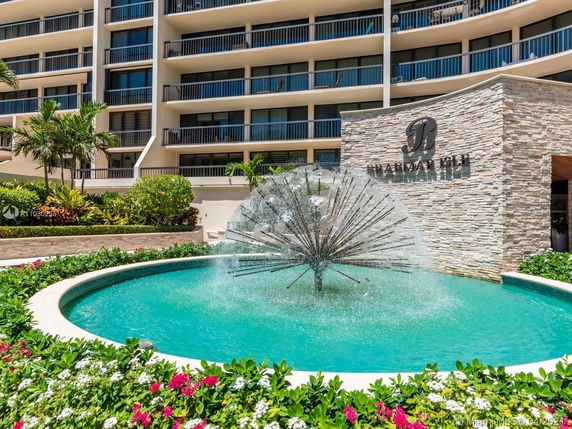 Front view of a multi-story building with balconies and a fountain in front.