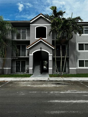 Front view of a multi-story building with a central staircase entrance and palm trees.