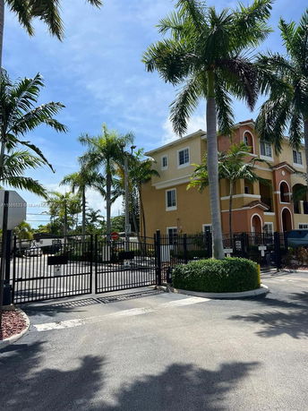 Front view of a three-story building with palm trees and a gated entrance.