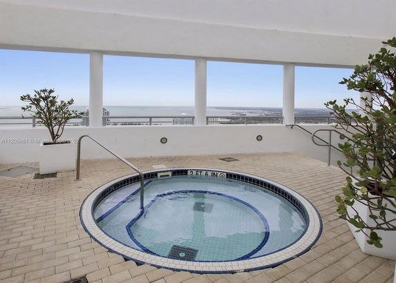 Rooftop view with a small round pool, railing, and plants overlooking a distant cityscape.