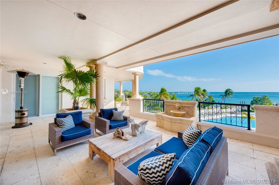 Outdoor patio area with wicker furniture and blue cushions, overlooking a pool and ocean view.