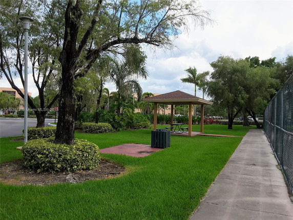 Outdoor area with a small pavilion and picnic table surrounded by grass and trees.