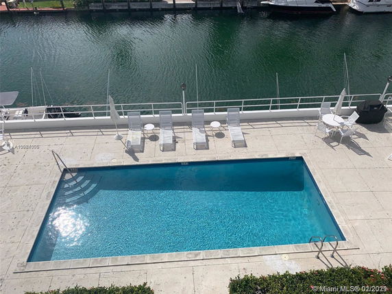 Outdoor swimming pool with surrounding deck and lounge chairs next to a body of water with boats.