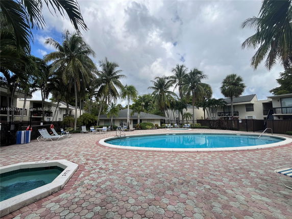Outdoor swimming pool area with lounge chairs and palm trees around.