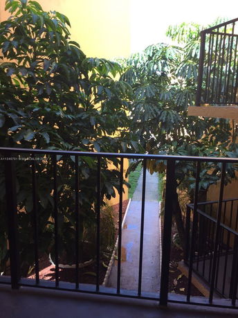 View from a balcony with railings overlooking a narrow pathway and dense greenery.