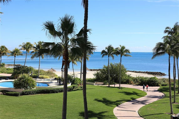 View of a pool and beach area with palm trees and ocean in the background.