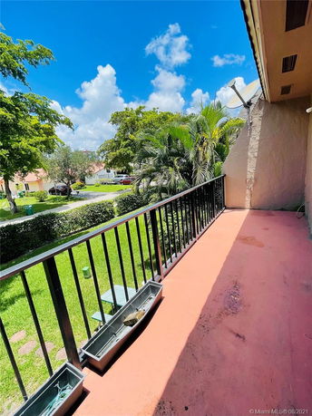 View from a balcony overlooking a grassy yard with trees and residential buildings.
