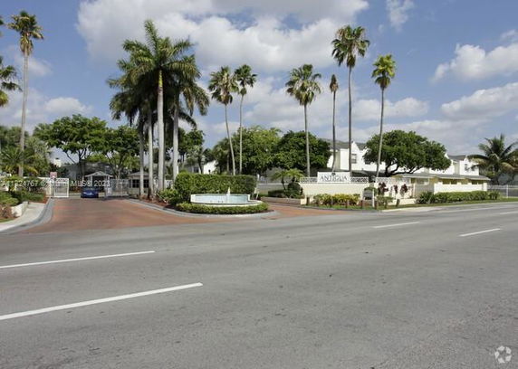Front view of a residential complex with palm trees and a sign at the entrance.