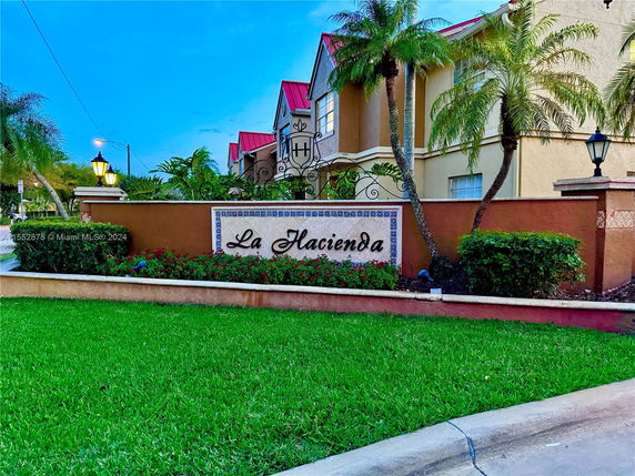 Front view of a residential building with La Hacienda sign and palm trees.