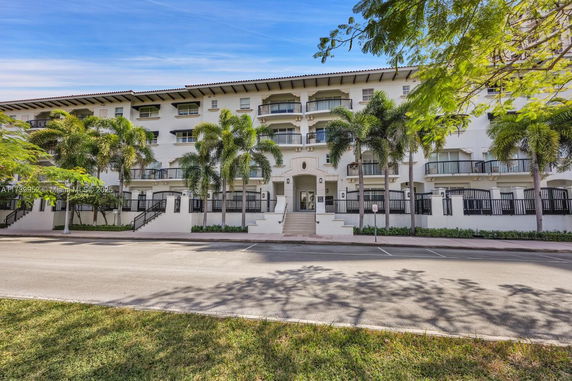 Front view of a multi-story building with balconies and palm trees.