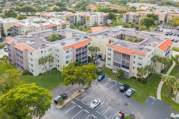 Aerial view of a residential building with flat rooftops featuring air conditioning units, surrounded by parking and greenery.