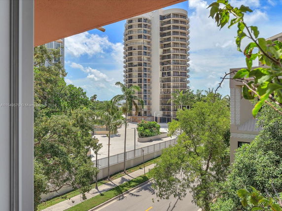 View of a tall, round building with balconies, seen from a nearby window.