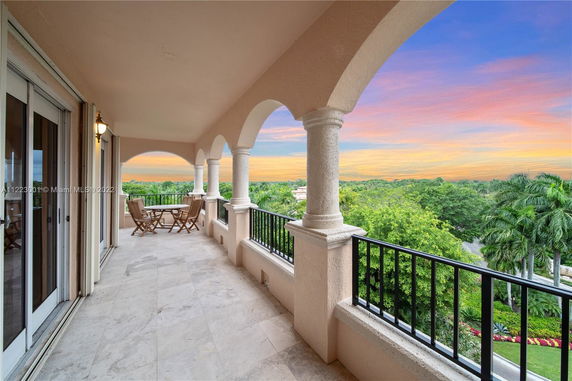 View from a balcony with patio furniture and an arch design overlooking greenery and a sunset sky.