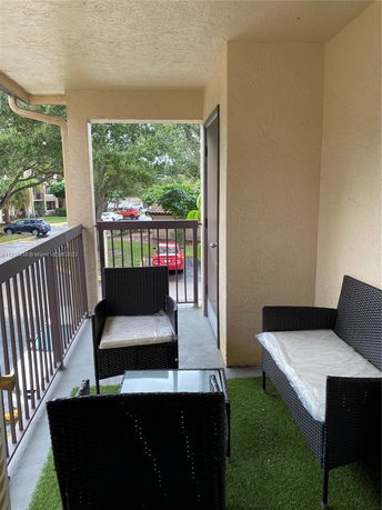 Outdoor seating area on a balcony with a view of trees and parked cars.