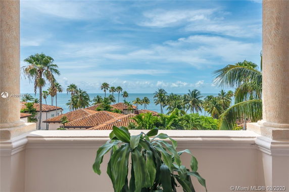Panoramic view of red-tiled rooftops with palm trees in the background, overlooking the ocean.
